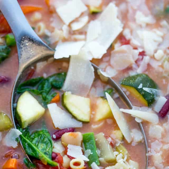 minestrone soup in ladle with fresh parmesan cheese on top