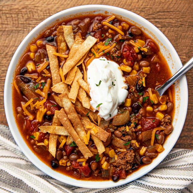 Bowl of Slow Cooker Taco Soup with tortilla strips, sour cream and cheese on wooden board